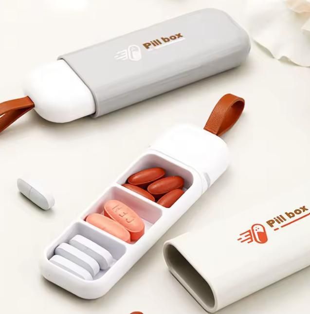 Pill box organizer with compartments containing pills on a white background, Pill organizer with three compartments showing plastic construction and small size perfect for daily medicine management