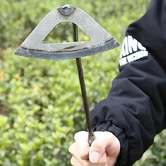 Person holding a metal tool with a triangular blade against a blurred green background. Durable manual weed puller with stainless steel blade demonstrating multiple uses including weeding and trenching